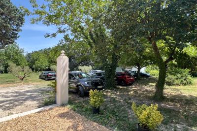Maison avec terrasse entourée de végétation, située dans un jardin avec allée en gravier et ciel dégagé en arrière-plan.