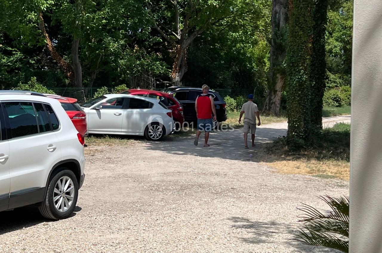 Deux personnes marchent sur un chemin gravillonné entouré de voitures stationnées et d'arbres.