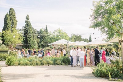Miniature Location salle Meyrargues (Bouches-du-Rhône) - Château de Vauclaire #8 Groupe de personnes assises et discutant dans un jardin ensoleillé avec des parasols blancs.