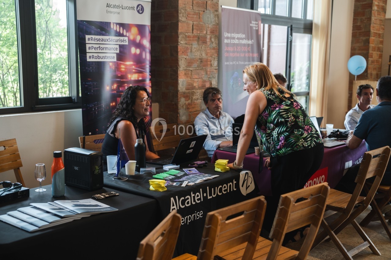 Des personnes discutent à un stand d'entreprise dans un espace intérieur avec des affiches et des brochures.