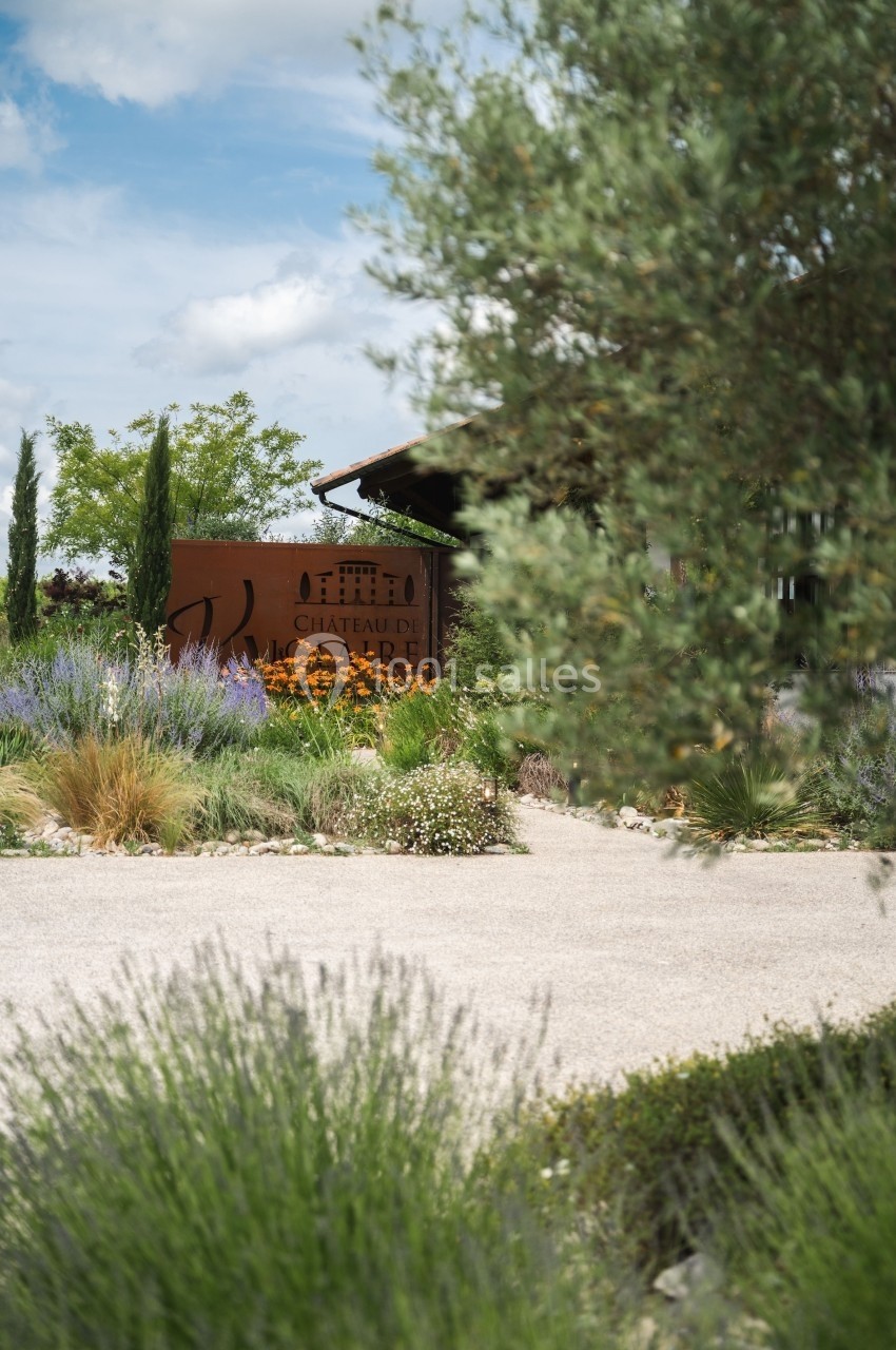 Jardin méditerranéen avec lavandes et arbustes, devant un panneau indiquant ’Château d'Aire’.