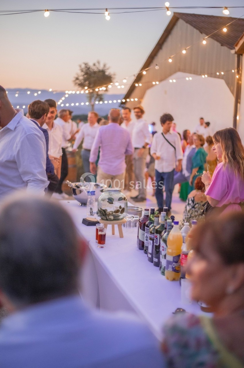 Groupe de personnes réunies en extérieur au coucher du soleil, avec une table de boissons au premier plan.