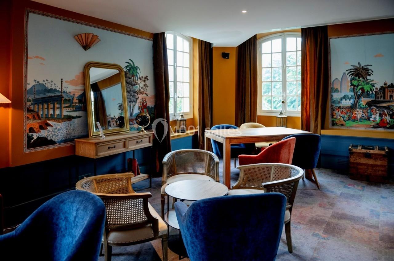 Salle lumineuse avec décoration vintage, chaises en osier, table en bois et fresques murales colorées.