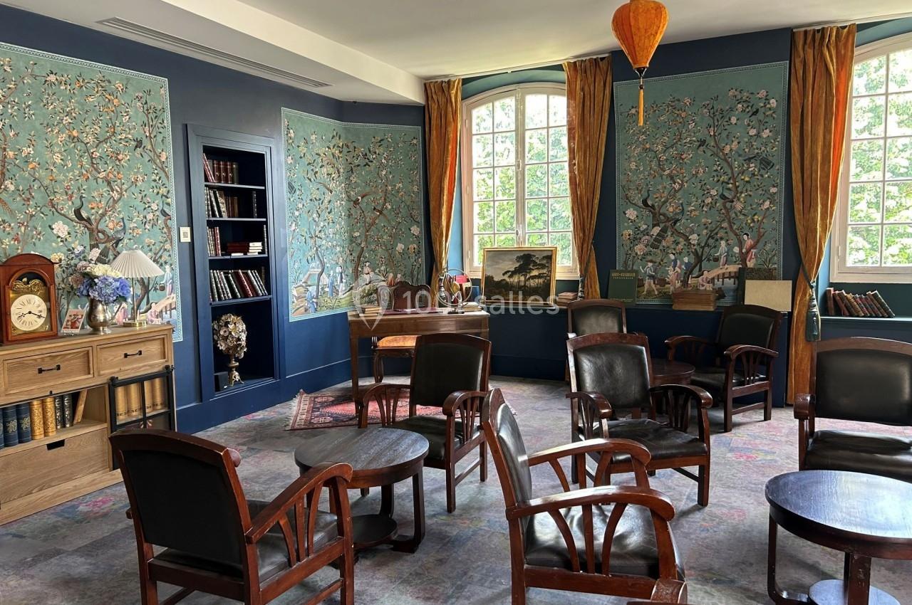 Salle de lecture lumineuse avec fauteuils en bois, bibliothèque, bureau et murs ornés de motifs floraux.