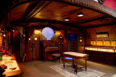 Salle lumineuse avec parquet, tapis décoré, fresques murales, rideaux sombres et plafond orné d'une carte céleste.