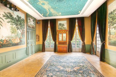 Salle lumineuse avec parquet, tapis décoré, fresques murales, rideaux sombres et plafond orné d'une carte céleste.