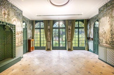 Salle lumineuse avec parquet, tapis décoré, fresques murales, rideaux sombres et plafond orné d'une carte céleste.