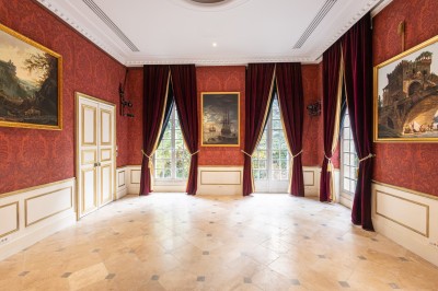 Salle lumineuse avec parquet, tapis décoré, fresques murales, rideaux sombres et plafond orné d'une carte céleste.