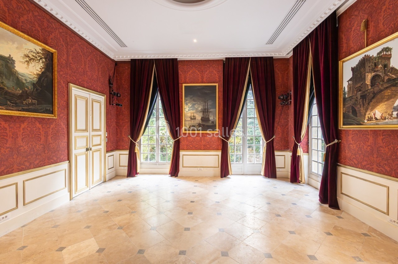 Salle élégante avec murs rouges ornés de tableaux, grandes fenêtres cintrées et rideaux pourpres encadrant la lumière…
