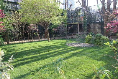 Salle lumineuse avec grandes baies vitrées ouvertes sur un jardin verdoyant, tables et chaises en métal.