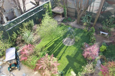Salle lumineuse avec grandes baies vitrées ouvertes sur un jardin verdoyant, tables et chaises en métal.