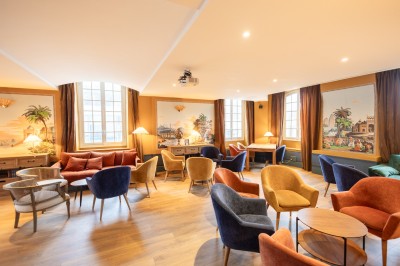 Salle lumineuse avec grandes baies vitrées ouvertes sur un jardin verdoyant, tables et chaises en métal.