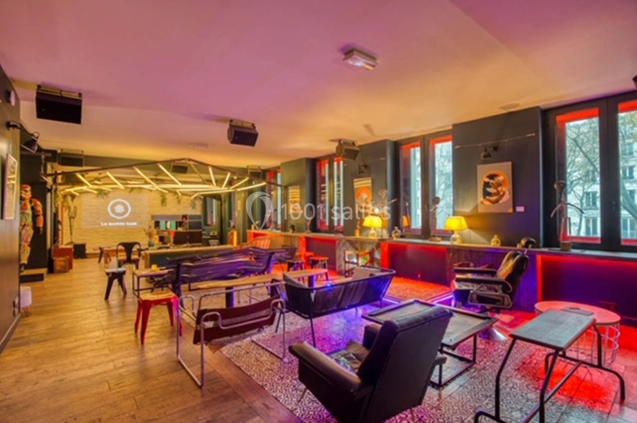 Salle moderne avec mobilier éclectique, éclairage coloré et grandes fenêtres donnant sur l'extérieur.