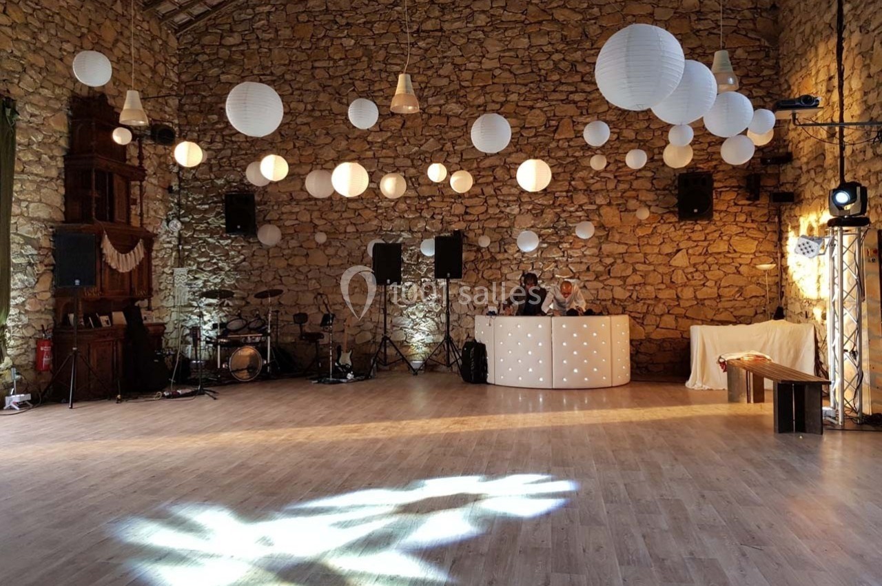 Salle en pierre avec parquet, décorée de lanternes suspendues, éclairée pour un événement avec une table de DJ.