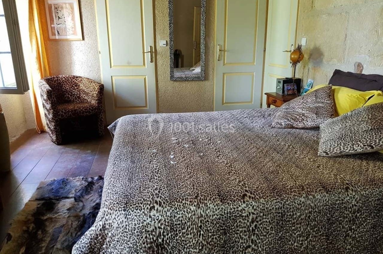 Chambre avec lit recouvert d'un couvre-lit à motif léopard, fauteuil assorti et miroir encadré sur un mur clair.