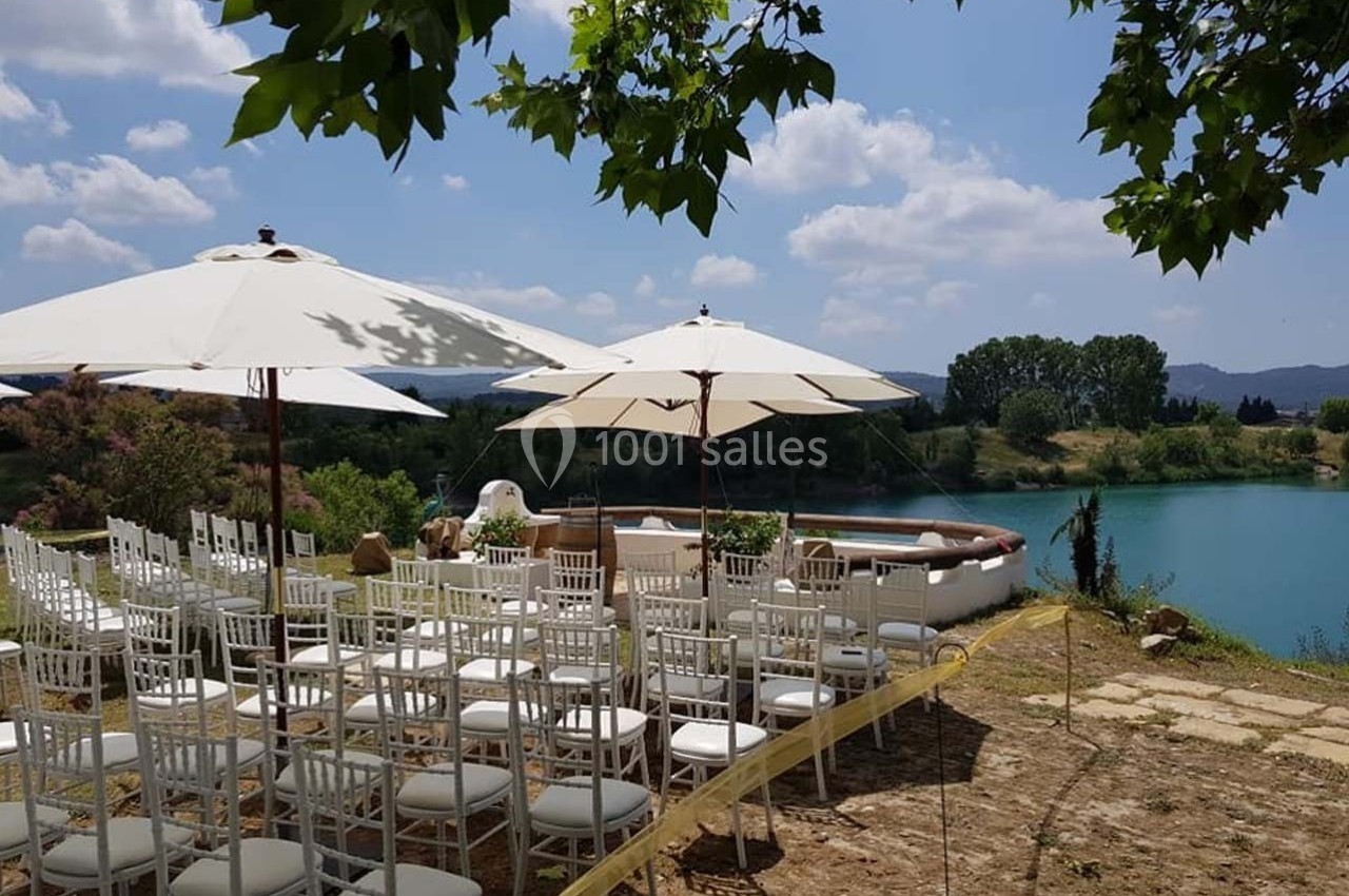 Chaises blanches alignées sous des parasols près d'une piscine, avec vue sur un lac et des arbres sous un ciel dégagé.