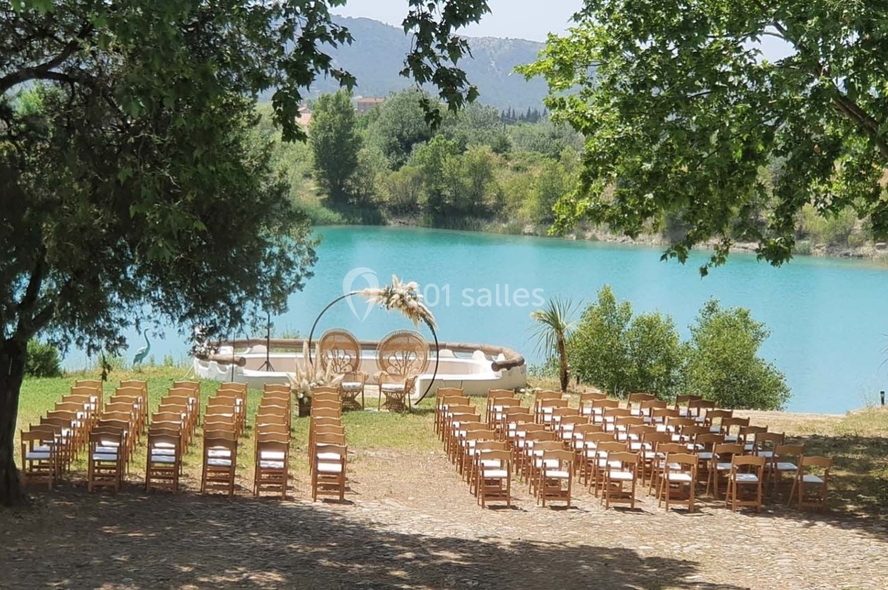 Chaises disposées en rangées face à une arche décorée près d'un lac turquoise, entouré de verdure.