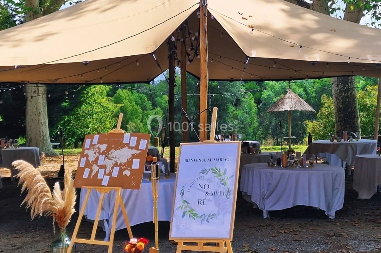 Tente beige en extérieur avec tables décorées, panneaux de bienvenue et plan de table sur chevalets.