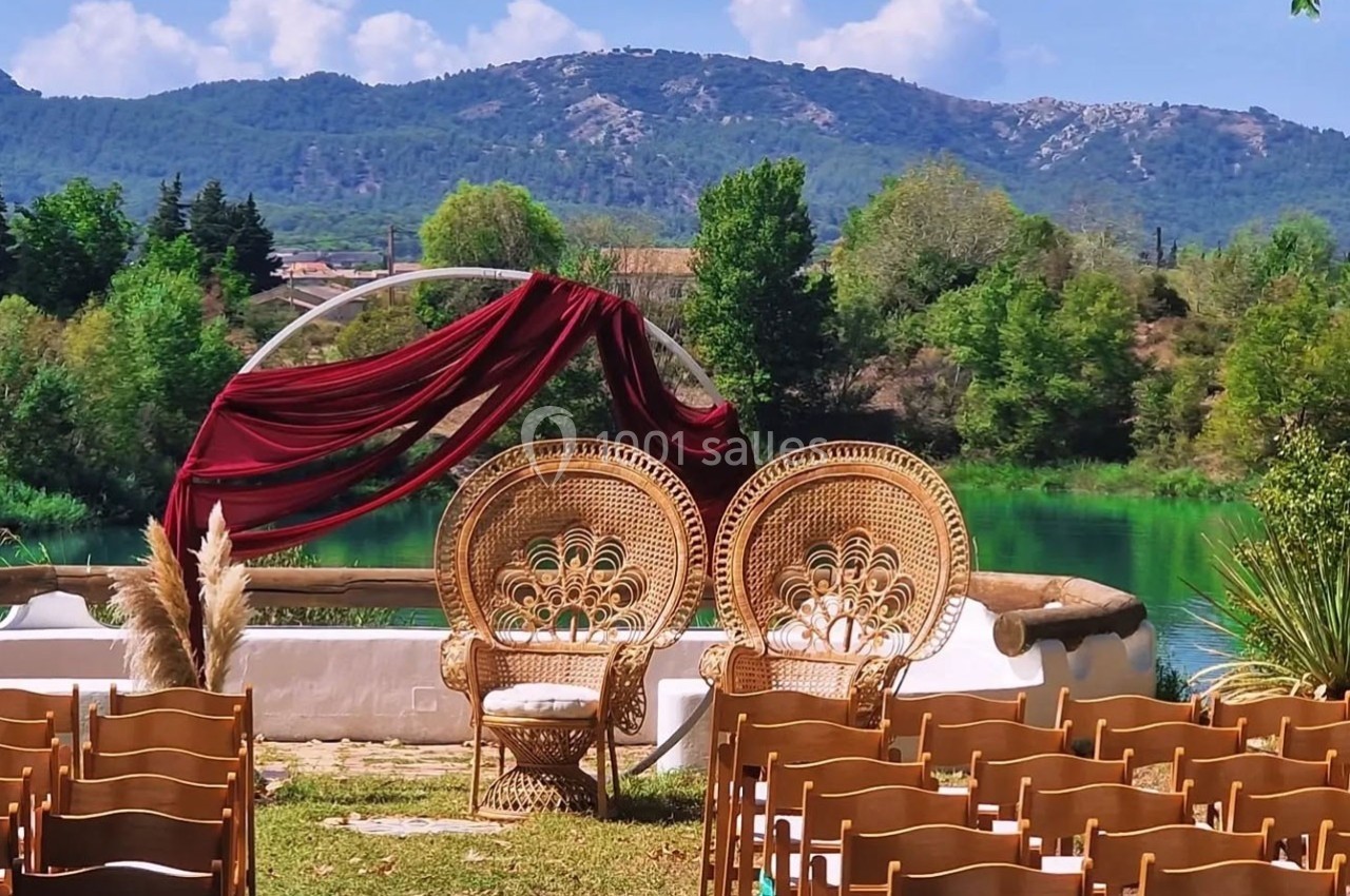 Chaises en bois disposées face à une arche décorée de tissu rouge, avec un lac et des collines verdoyantes en arrière-plan.