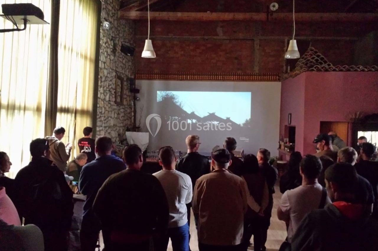 Un groupe de personnes regarde une projection sur un écran dans une salle avec murs en pierre et plafond en bois.