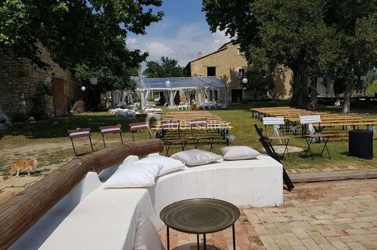 Espace extérieur avec tables, chaises et canapé, entouré de verdure et bâtiments en pierre sous un ciel dégagé.