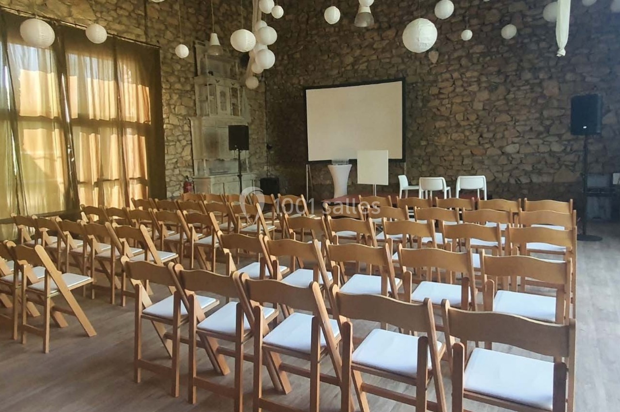 Salle en pierre aménagée pour une présentation, avec des rangées de chaises en bois face à un écran de projection.