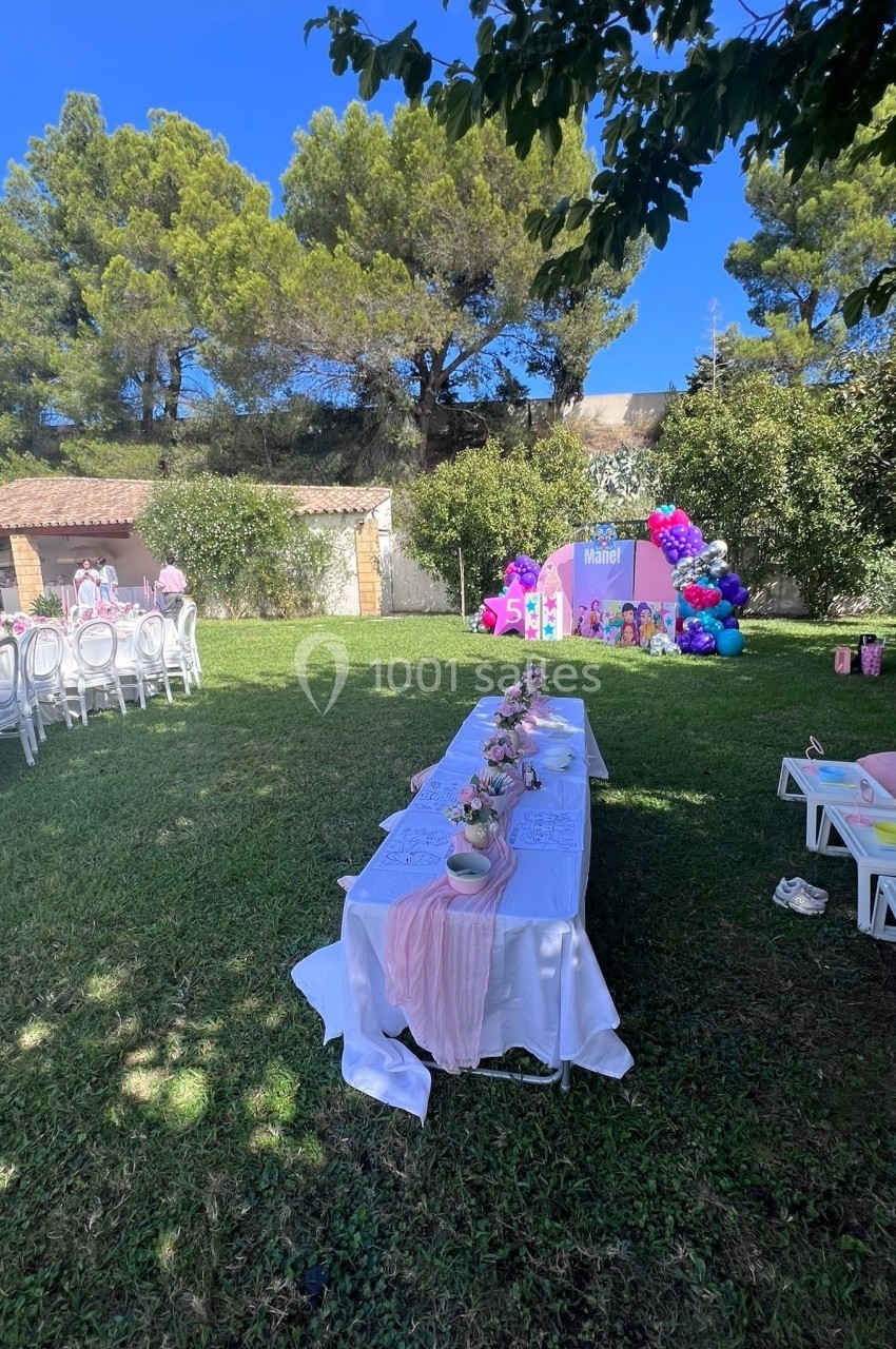 Tables décorées pour une fête en plein air avec nappes blanches, décorations roses et ballons colorés dans un jardin…