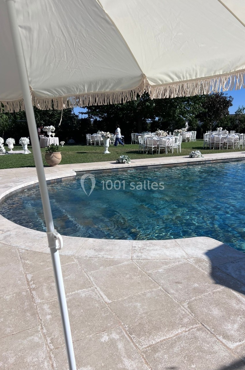 Vue d'une piscine entourée de chaises blanches et de décorations florales, avec un parasol au premier plan.