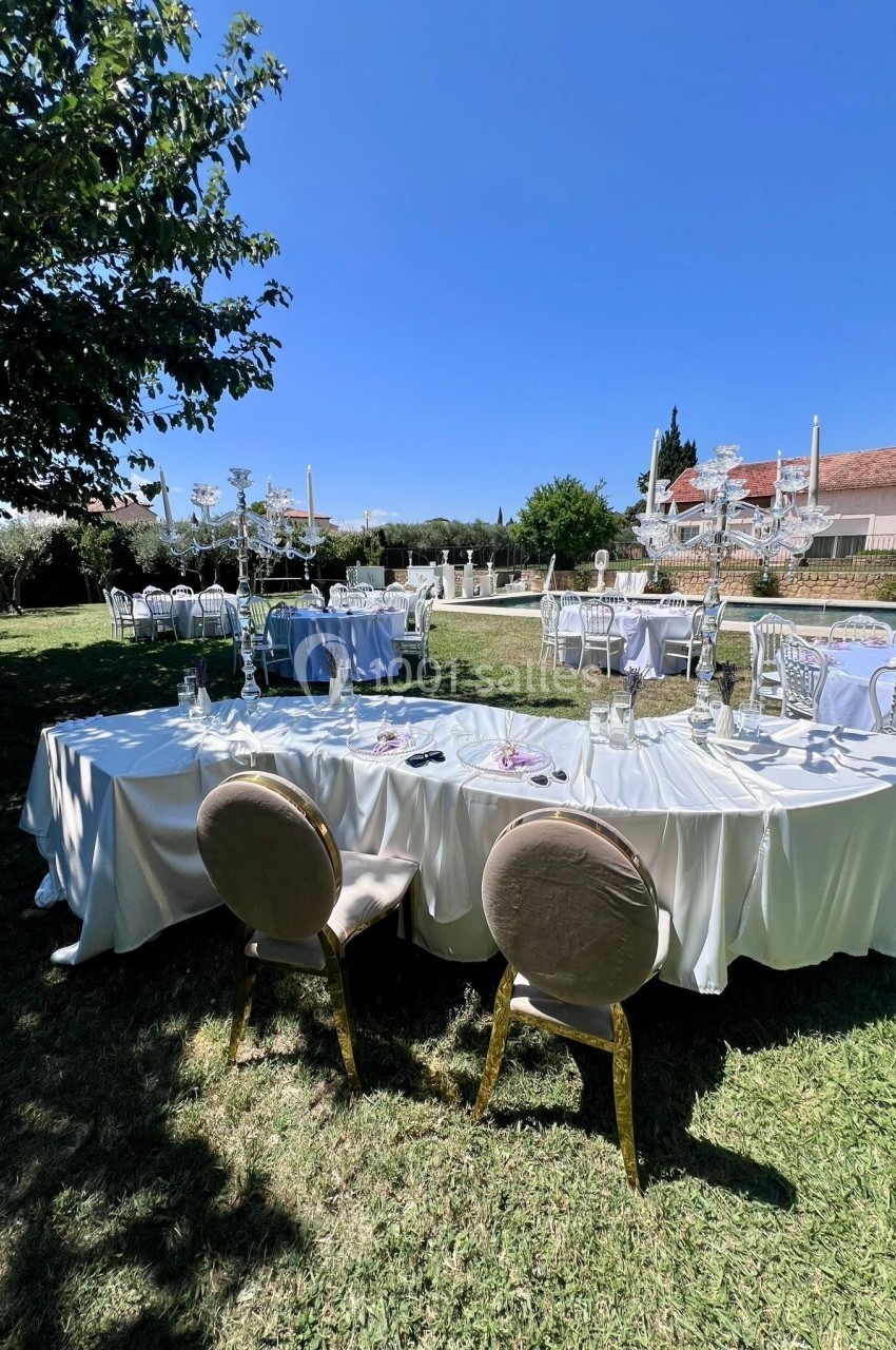Tables rondes et rectangulaires dressées en extérieur sur une pelouse, sous un ciel bleu, près d'un bâtiment.