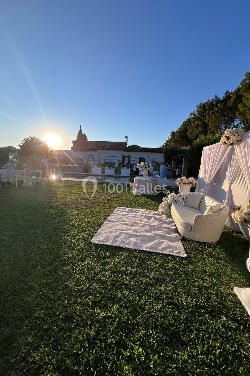 Espace extérieur décoré pour un événement avec canapé, fleurs blanches et tables, au coucher du soleil.