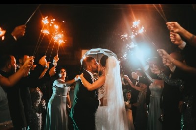 Un couple s'embrasse sous une arche, entouré d'invités tenant des cierges magiques allumés dans l'obscurité.