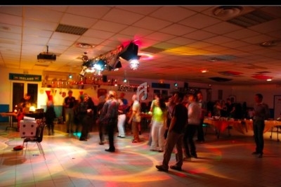 Des personnes dansent dans une salle éclairée par des lumières colorées, avec des tables en arrière-plan.