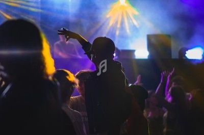 Personnes dans une ambiance festive, éclairées par des lumières colorées et des projecteurs dans une salle sombre.