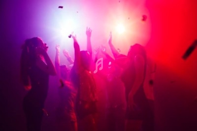 Groupe de personnes dansant sous des lumières colorées rouge et violette dans une ambiance festive.