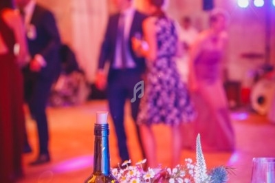 Bouteille décorative et fleurs sur une table, avec des invités dansant en arrière-plan dans une ambiance festive.