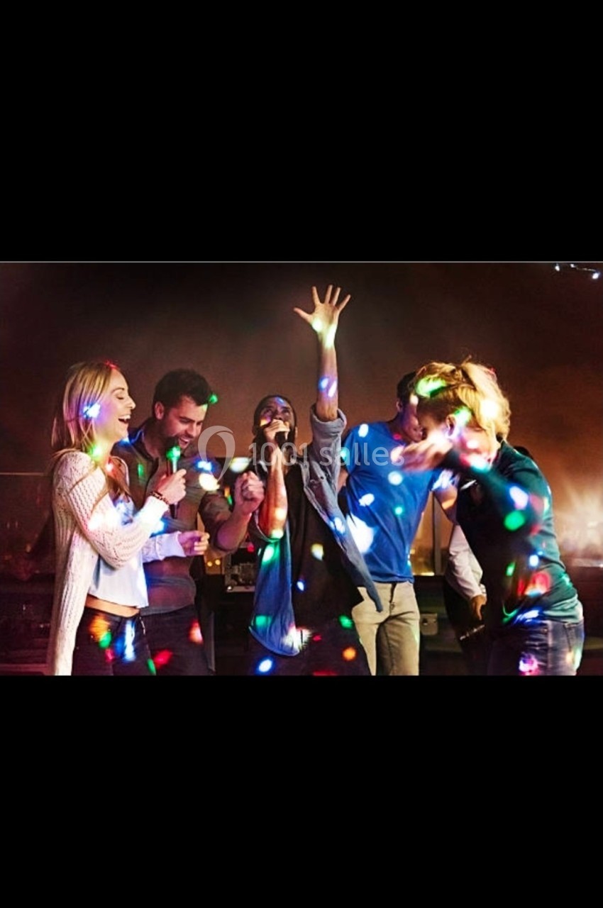 Des personnes chantent et dansent sous des lumières colorées dans une ambiance festive.