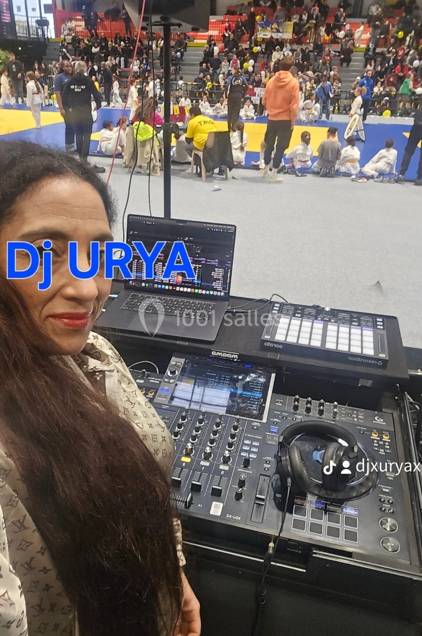 Femme devant une table de mixage avec ordinateurs, dans une salle où se déroule un événement sportif ou culturel.