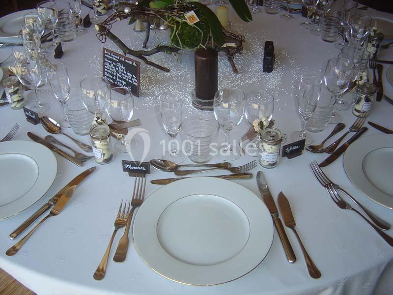 Table dressée avec vaisselle élégante, couverts en métal, verres alignés et décorations florales au centre.