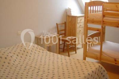 Chambre avec un lit double, une lampe de chevet allumée, un lit superposé en bois et un mur peint en rose pâle.