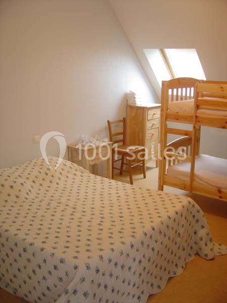 Chambre simple avec un lit double, des lits superposés en bois, une chaise, une commode et une fenêtre de toit.