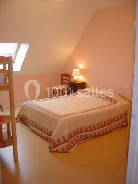 Chambre avec un lit double, une lampe de chevet allumée, un lit superposé en bois et un mur peint en rose pâle.