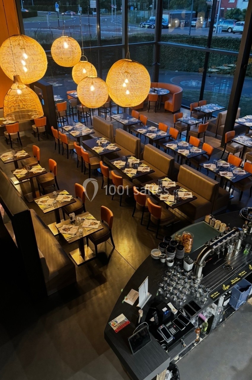 Vue d'ensemble d'un restaurant moderne avec tables dressées, banquettes orange et grand bar en premier plan.