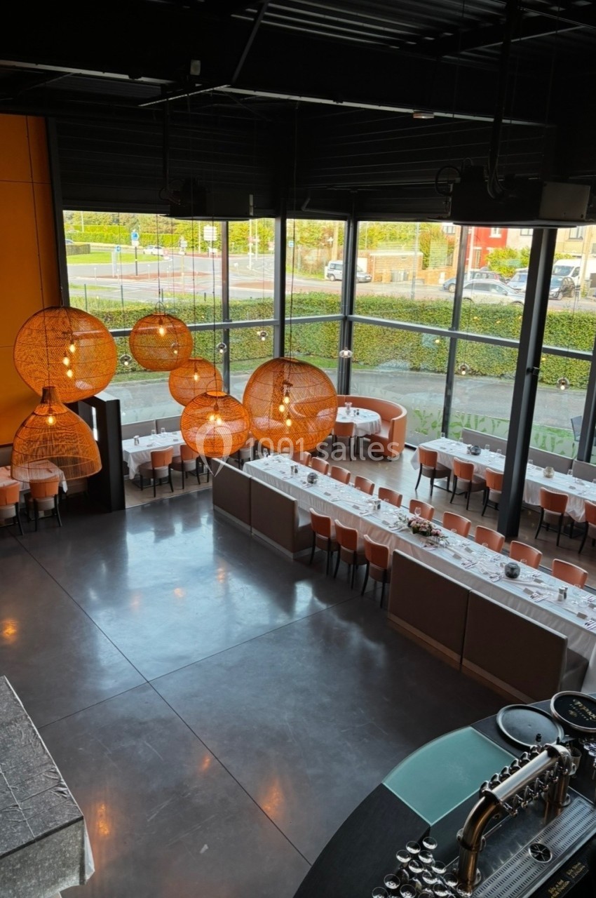 Vue d'un restaurant moderne avec de grandes baies vitrées, des tables dressées et des luminaires suspendus en osier.