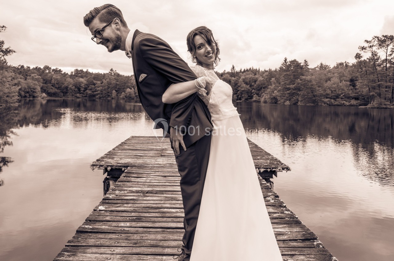 Un couple en tenue de mariage se tient dos à dos sur un ponton en bois au bord d'un lac entouré de forêt.