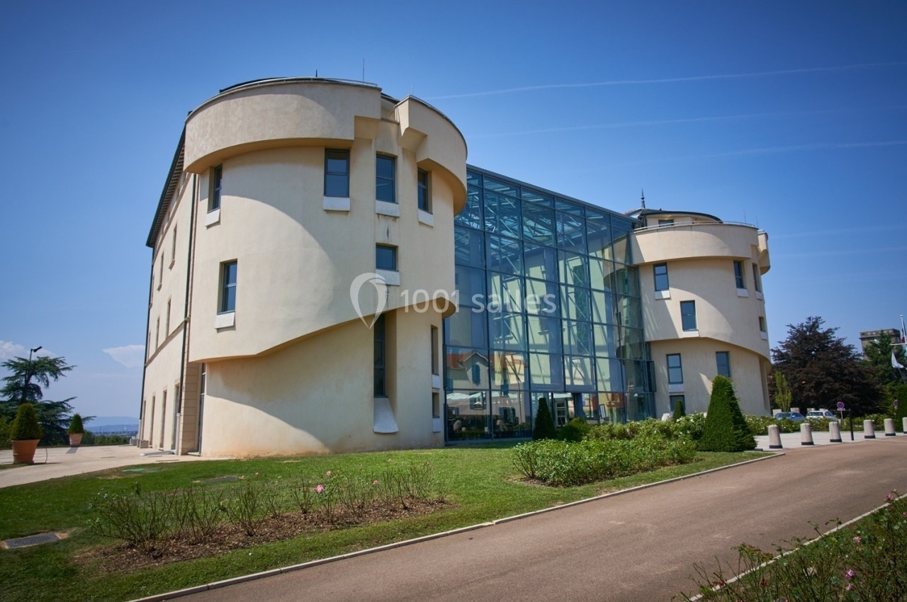 Bâtiment moderne avec façades arrondies et une grande verrière, entouré de pelouse et d'allées.