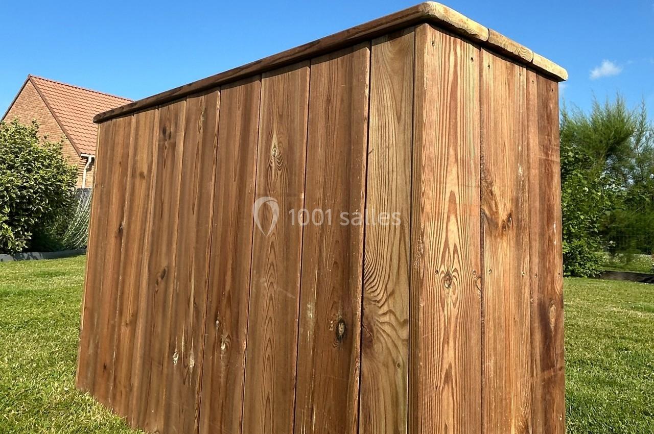 Coffre en bois massif posé sur une pelouse, entouré de végétation et d'une maison en arrière-plan.