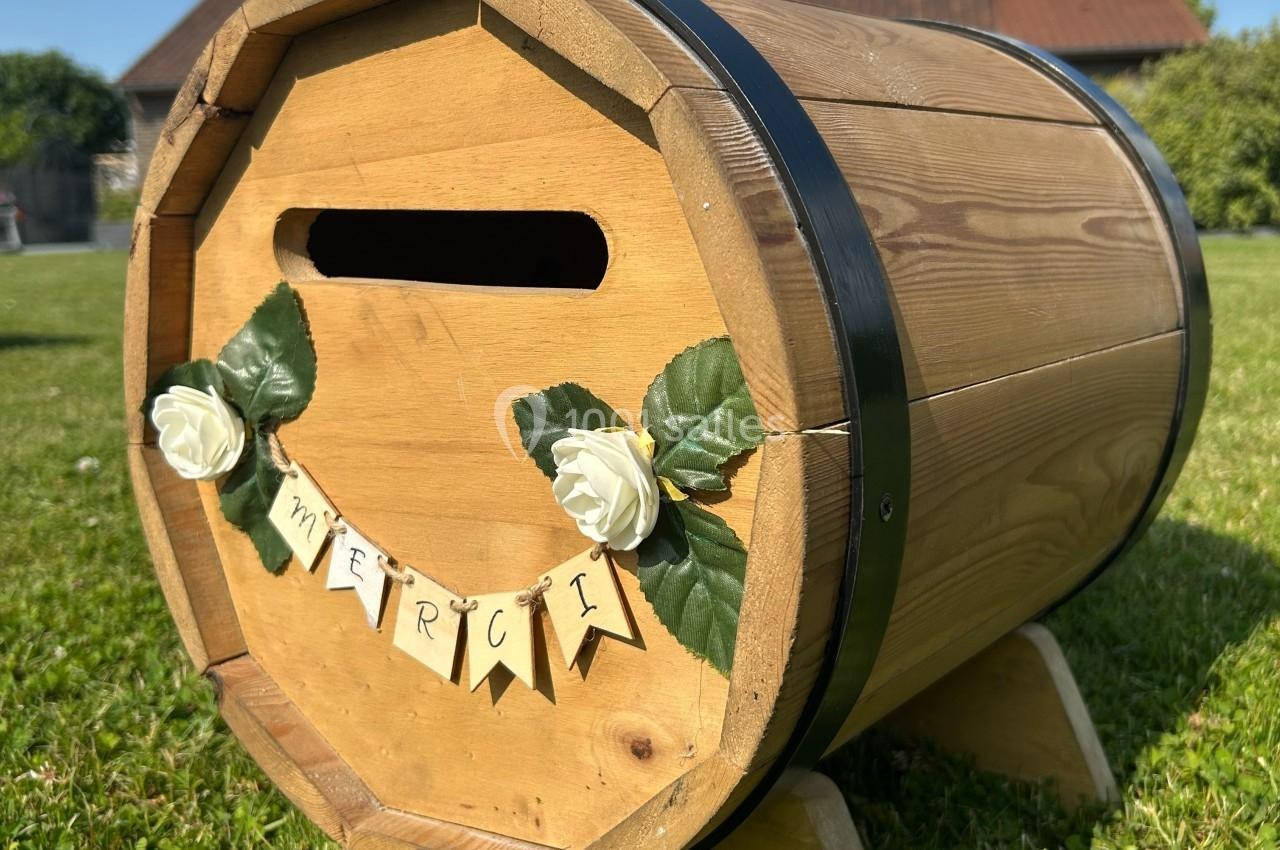 Tonneau en bois transformé en urne avec une fente, décoré de roses blanches et d'une guirlande ’merci’.