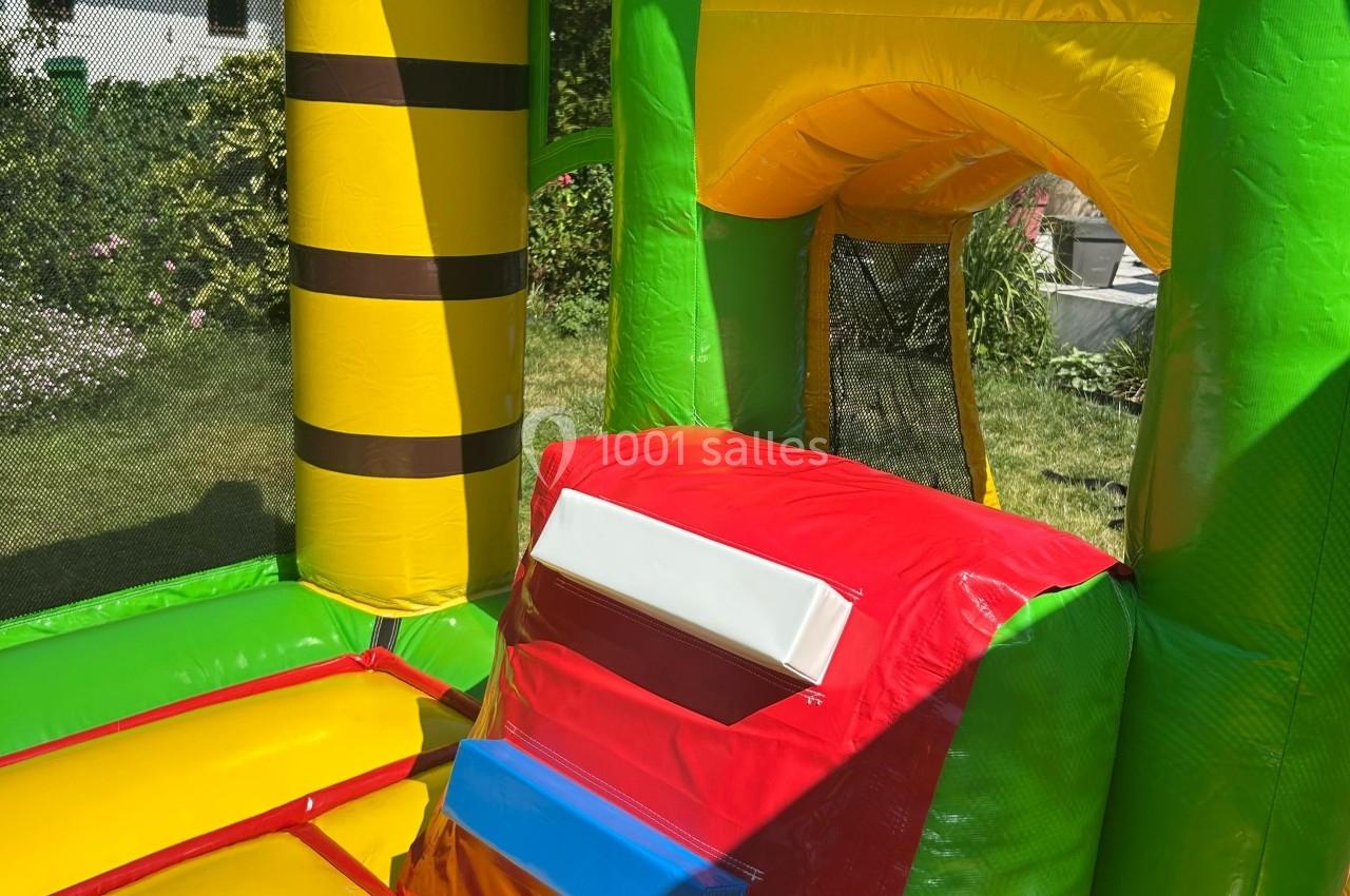 Structure gonflable colorée avec toboggan et filet de sécurité, installée dans un jardin ensoleillé.