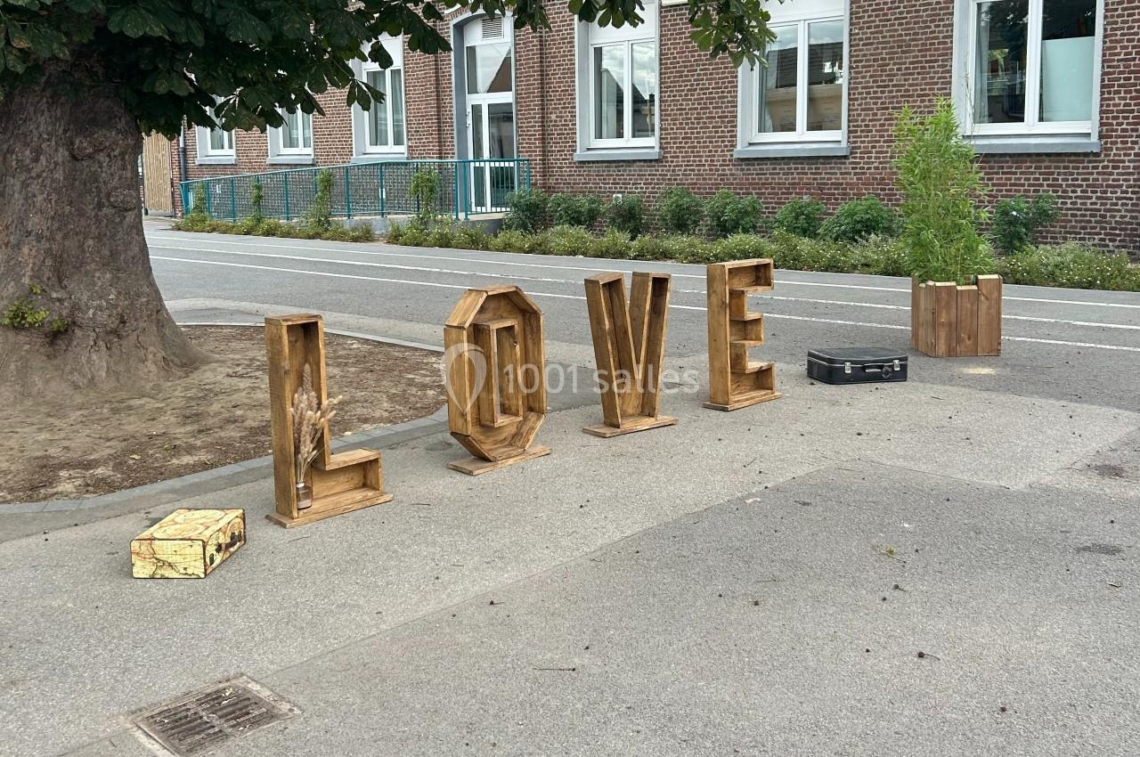 Lettres en bois formant le mot ’LOVE’ disposées sur un trottoir près d'un arbre et d'un bâtiment en briques.