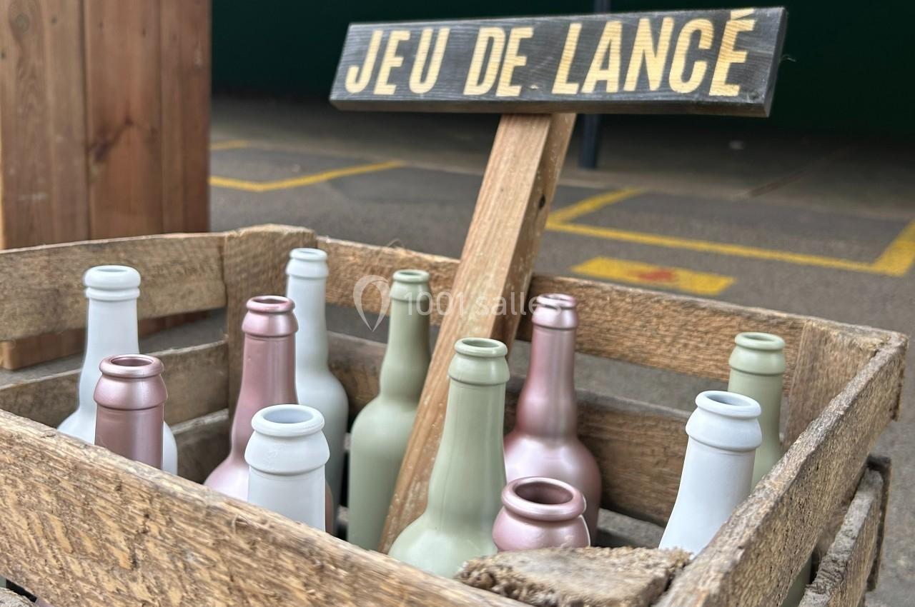 Caisse en bois contenant des bouteilles colorées, avec un panneau indiquant ’Jeu de lance’ en arrière-plan.